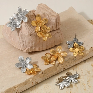 Detail of flower-shaped earrings in gold and silver finish on natural stone background