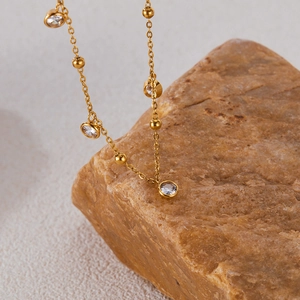 Detail of gold necklace with zircon pendants draped over a natural brown stone