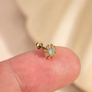 Puce d'oreille fleur en or avec opale et cristaux tenue sur le bout du doigt