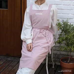 Pink breathable cotton apron with neck strap and front pocket shown in outdoor garden
