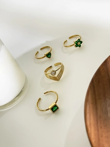 Détail de quatre bagues dorées ajustables avec cristaux vert émeraude et pierres zircon