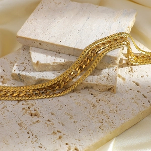 Macro detail of 18K gold-plated curb and herringbone chains on travertine stone