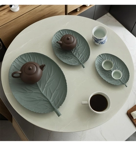 Detailed view of three sizes of matte green leaf-shaped iron trays on marble background