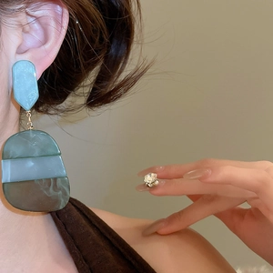 Detailed close-up of long oval resin drop earrings in green tones on a female model