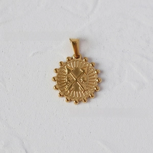 Macro shot of 18K gold plated coin pendant with crossed arrows and beaded edge