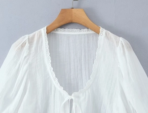 Détail du chemisier blanc à col en V avec bordure en dentelle et fermeture à nouer