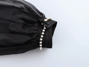 Detail of sheer black organza shirt cuff featuring elegant pearl beads and button