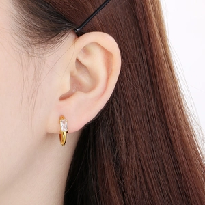 Gros plan d'une boucle d'oreille en acier doré avec pierre rectangulaire transparente