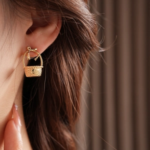Close-up of a golden flower basket earring with bow detail worn by a female model