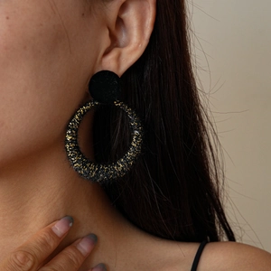 Detail of black velvet hoop earrings with golden glitter finish worn by a model