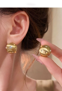 Close-up of matte gold sphere earrings with brushed metal finish and star-shaped zircons