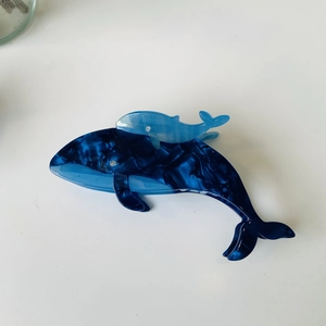 Detail of whale-shaped acetate hair claw with blue marble texture and 3D dolphin accent