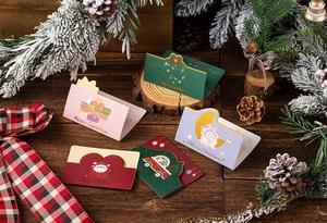 Detailed view of assorted Christmas folding cards on a festive wooden table with pine cones