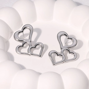 Triple hollow heart drop earrings in silver stainless steel on a white ceramic tray