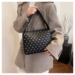 Chic rivet shoulder bag in black faux leather held by a model in a beige blazer