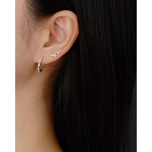 Detailed close-up of U-shaped silver hoop and leaf stud earrings on a model