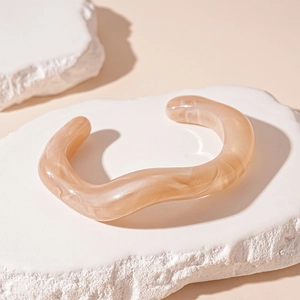 Macro detail of amber resin cuff bracelet with marble texture on a white stone tray