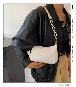 Detail of white baguette bag with crocodile texture and resin chain strap on black jacket
