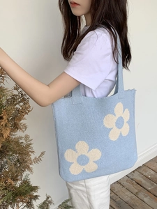Blue knitted tote bag with white flower patterns shown on a model's shoulder