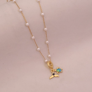 Close-up of golden necklace featuring a sea turtle, whale tail pendant, and white pearls