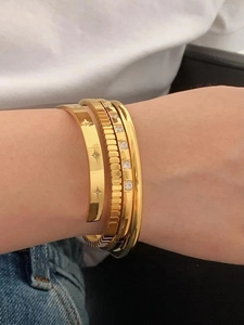 Detailed close-up of three layered 18K gold-plated titanium steel bangles on a wrist