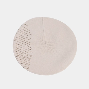 Détail du béret en maille beige avec rangées de clous métalliques dorés décoratifs