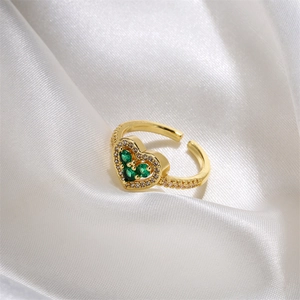 Dettaglio anello cuore dorato con zirconi verde smeraldo su sfondo di seta bianca
