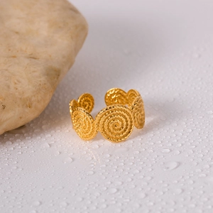 Detailed view of a gold spiral textured adjustable ring on a white surface with water drops