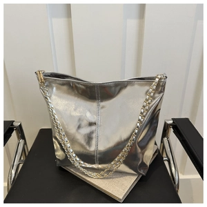 Silver tote bag with glossy metallic finish and gold chain strap on a black chair
