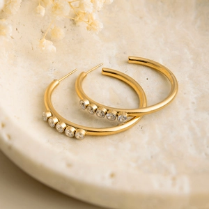 Detail of 18K gold-plated stainless steel hoop earrings with five clear zircons on stone tray