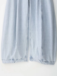 Detail van een lichtblauwe balloon jeans met gewassen textuur en verticale stiksels