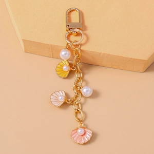Close-up of golden keychain featuring yellow and pink shell charms with imitation pearls