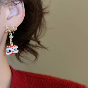 Close-up of golden bow earring with traditional lion dance pendant and white pearl details