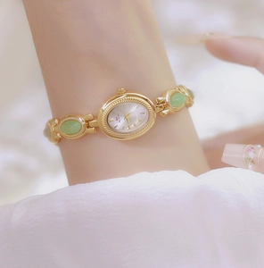 Close-up of elegant gold chain watch with green gemstone inlay on woman's wrist