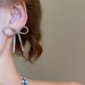 Gros plan de boucles d'oreilles nœuds gris translucides portées dans un style minimaliste