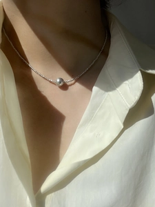 Close-up of a silver stainless steel beaded necklace with a central orb on a model
