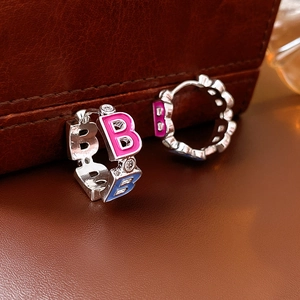 Detailed view of silver hoop earrings with pink and blue enamel B letters and zircon