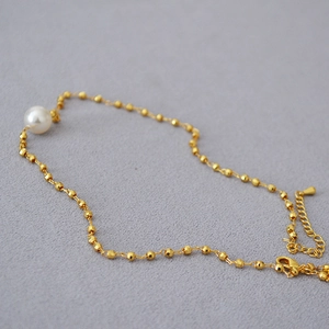 Macro detail of a 14k gold plated brass chain with a single white pearl and lobster clasp