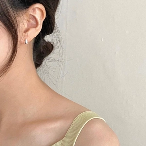 Close-up of minimalist silver water drop stud earring worn by a model in soft light