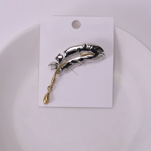 Detailed silver feather brooch with gold teardrop pendant on a white jewelry card