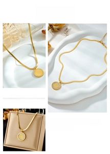 Macro detail of a golden coin pendant on a flat snake chain against a marble background