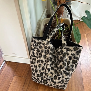 Detail of plush leopard print tote bag with metal label on wooden floor and green plant