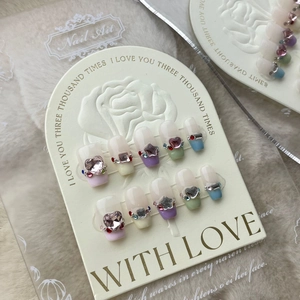 Detailed close-up of press-on nails featuring pink heart rhinestones and French gradient