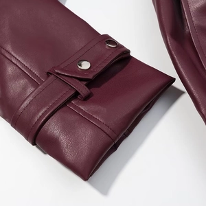 Détail de la manche d'un manteau long en similicuir bordeaux avec boutons argentés