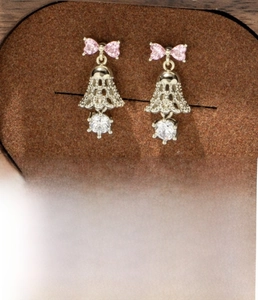 Detailed view of pink bow and hollow bell pendant earrings with zircon insets