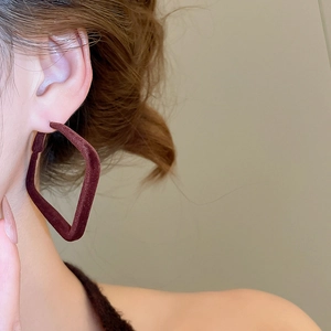 Gros plan d'un modèle portant des boucles d'oreilles losanges floquées marron foncé