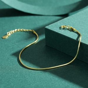 Minimalist gold snake bone chain bracelet with lobster clasp on dark background