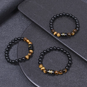 Détail de bracelets en œil de tigre et obsidienne avec breloques lettres dorées
