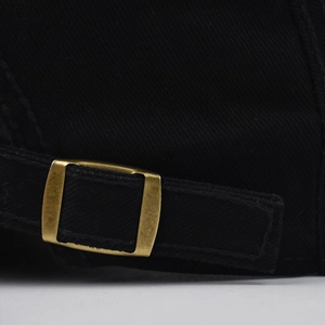 Detail of adjustable brass metal buckle on black cotton twill flat cap for men