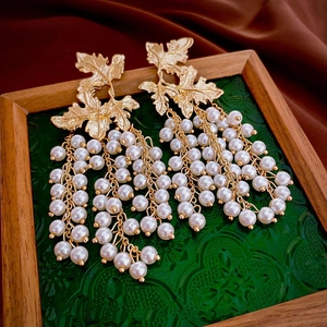 Macro detail of gold maple leaf earrings with white imitation pearl fringe tassels